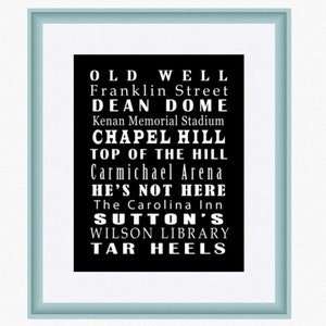 Op de afbeelding: Zwart-wit typografieprint met de tekst "Old Well", "Franklin Street", "Dean Dome", "Kenan Memorial Stadium", "Chapel Hill", "Top of the Hill", "Carmichael Arena", "He's Not Here", "The Carolina Inn", "Sutton's", "Wilson Library" en "Tar Heels".