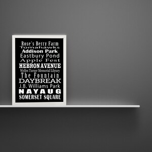 May include: Black and white framed print with a list of places and events in white text on a black background. The text includes: Rose's Berry Farm, Tomahawks, Addison Park, Eastbury Pond, Apple Fest, Hebron Avenue, Welles Turner Memorial Library, The Fountain, Daybreak, J.B. Williams Park, Nayaug, Somerset Square.