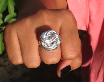 Könnte beinhalten: Ein silberner Ring mit einem Knotendesign. Der Ring wird an einem Finger getragen.