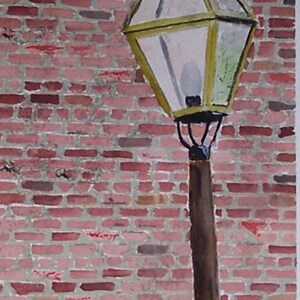 May include: Watercolor painting of a street lamp with a yellow-green glass lantern and a brown pole. The lamp is in front of a red brick wall. A window is visible at the top. The artist's signature is at the bottom.