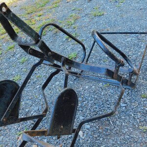 K&ouml;nnte beinhalten: Schwarzer Metallrahmen mit zwei schwarzen Metallfu&szlig;st&uuml;tzen. Der Rahmen ist zusammengeklappt und scheint ein Vintage-Fahrradtr&auml;ger zu sein.