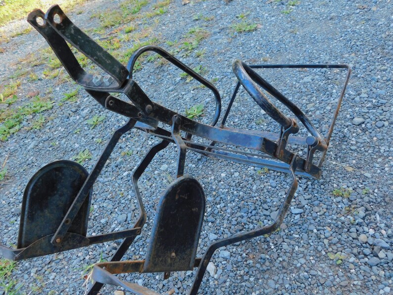 K&ouml;nnte beinhalten: Schwarzer Metallrahmen mit zwei schwarzen Metallfu&szlig;st&uuml;tzen. Der Rahmen ist zusammengeklappt und scheint ein Vintage-Fahrradtr&auml;ger zu sein.