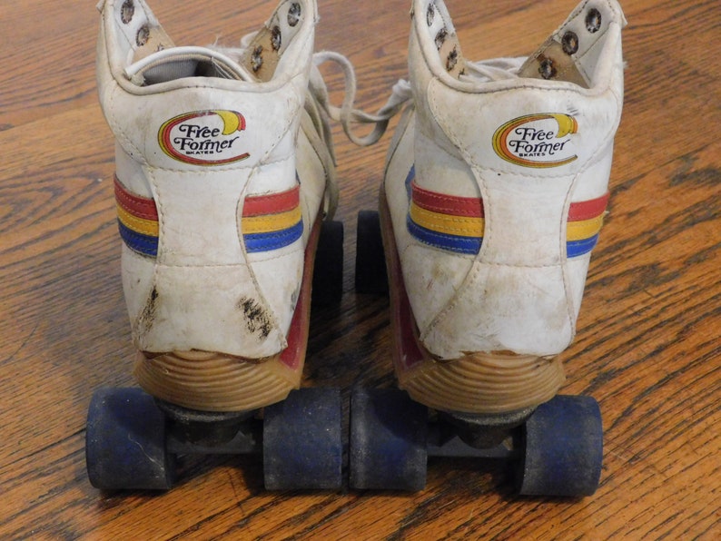 May include: A pair of white roller skates with blue, red, and yellow stripes. The skates have a Free Former logo on the back of each boot. The wheels are black with blue hubs.