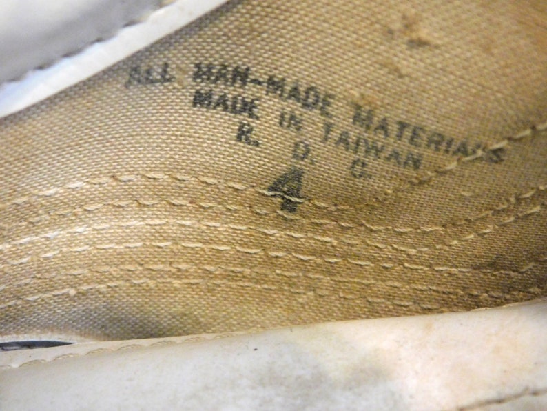 May include: Close-up of a white fabric shoe label with black text that reads "All Man-Made Materials Made in Taiwan R.O.C. 4".