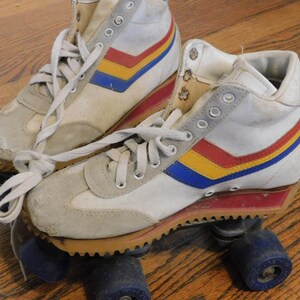 May include: A pair of white roller skates with red, yellow, and blue stripes. The skates have a high-top design and are worn.