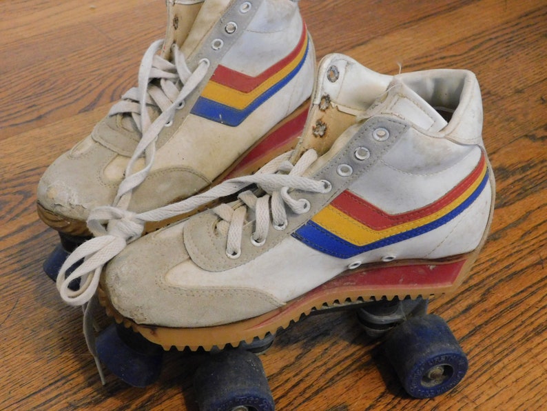 May include: A pair of white roller skates with red, yellow, and blue stripes. The skates have a high-top design and are worn.