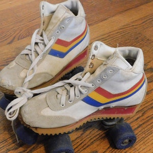May include: A pair of white roller skates with blue, yellow, and red stripes. The skates have white laces and blue wheels.