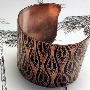 May include: A copper cuff bracelet with a black and copper woodgrain pattern. The bracelet is open on one side and has a smooth, polished finish.