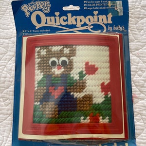 May include: A red plastic frame with a colorful needlepoint design of a bear with googly eyes. The package says "Peppers Quickpoint by Betty's" and "easy to do!" with a safety needle included.
