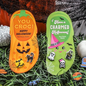 May include: Two Halloween-themed Croc shoe charms, one orange and one green, with various Halloween-themed charms. The orange charm says "You Croc! Happy Halloween!" and the green charm says "Have a Charmed Halloween!"