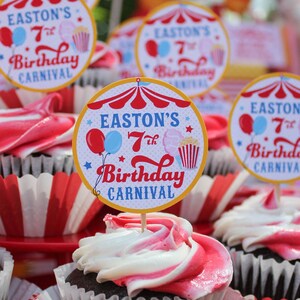 May include: A close-up of a table with cupcakes decorated with red and white frosting. Each cupcake has a round, colorful paper topper that says "Easton's 7th Birthday Carnival".