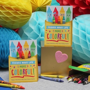 Op de afbeelding: Twee kleurrijke Valentijnsdagkaarten met krijtillustraties en de tekst "FRIENDS MAKE LIFE MORE COLORFUL!" Een doosje krijtjes ligt op de voorgrond.