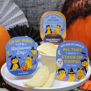May include: Three Halloween-themed chip bag toppers with cute illustrations of chip characters dressed as a vampire, cat, and witch. The text on the toppers reads "Chip Chip Hooray! It's Halloween Day!" "Hope your Halloween is All That and a Stack of Chips!" and "Chip or Treat! I see a great snack for you to eat!"