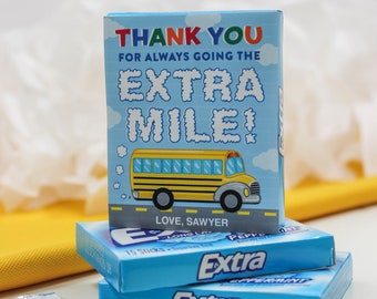 May include: A blue and yellow thank you card with a school bus illustration and the text "Thank you for always going the extra mile! Love, Sawyer". The card is sitting on top of two packs of Extra peppermint gum.
