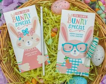 May include: Two Easter bunny gift tags with personalized messages. The tags feature a bunny with a pink dress and a bunny with glasses and a blue plaid shirt. The tags are in a wicker basket with pastel-colored Easter eggs and candy.
