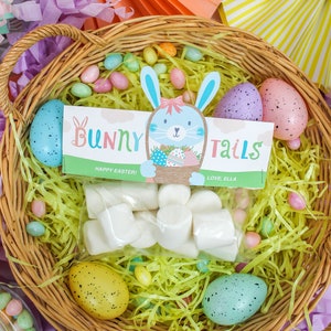 May include: A wicker basket filled with yellow shredded paper, pastel-colored jelly beans, and a bag of white marshmallows. There is a printable tag with the text "Bunny Tails" and a cute bunny illustration. The tag also says "Happy Easter!" and "Love, Ella".