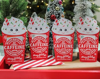 May include: Four red and white Christmas gift cards shaped like coffee cups with a white whipped cream top and red and green sprinkles. The cards have a cartoon face with a smiling expression. The text on the cards reads "My kids may be why you need caffeine. Enjoy some today!" and "Our kids may be why you need caffeine. Enjoy some on us!"