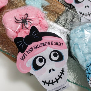 Puede incluir: Algod&oacute;n de az&uacute;car rosa y azul en bolsas transparentes con una pegatina de calavera rosa y blanca que dice "Espero que tu Halloween sea dulce" con un lazo negro y el texto "Love, Sawyer & Easton".
