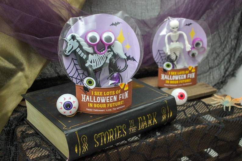 May include: Two Halloween-themed goodie bags with googly eyes and skeleton figures. The bags are on a book with the text "Stories in the Dark".