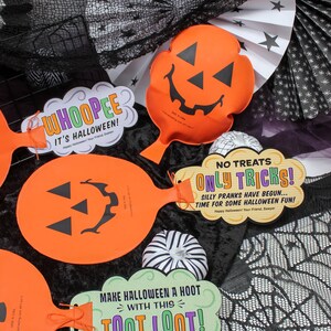 May include: Three orange pumpkin-shaped Halloween party favours with black jack-o'-lantern faces. Each favour has a different message: "Whoopie It's Halloween!", "No Treats Only Tricks! Silly Pranks Have Begun... Time For Some Halloween Fun!" and "Make Halloween A Hoot With This Toot Loot!"