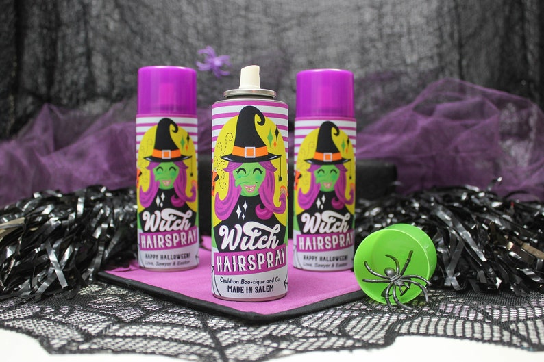 May include: Three purple and green Halloween themed hairspray cans with a witch graphic and the text "Witch Hairspray" and "Happy Halloween". The cans are on a black and white lace tablecloth with a green spider on a green plastic spider web.