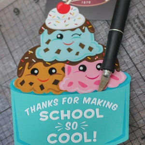 Puede incluir: Una tarjeta azul y blanca con una pila de conos de helado con caras. La tarjeta dice "Gracias por hacer la escuela tan genial! Con cari&ntilde;o, Sawyer".