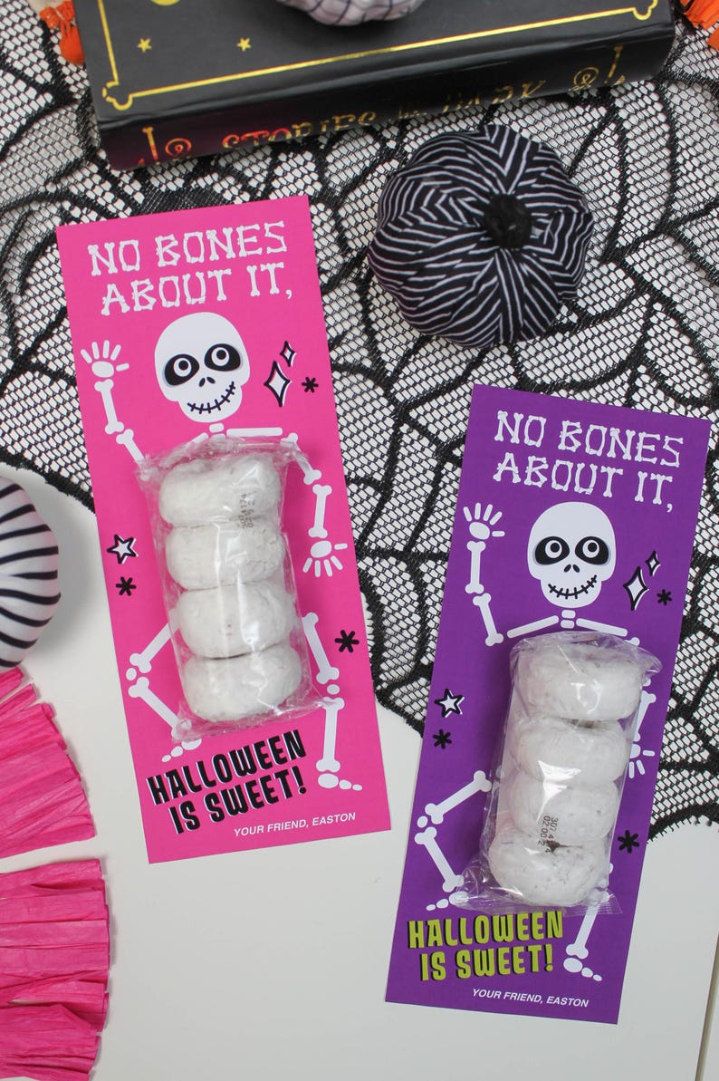 May include: Two pink and purple Halloween treat bags with a skeleton graphic and the text "No bones about it, Halloween is sweet!"  Each bag contains a stack of four mini donuts.