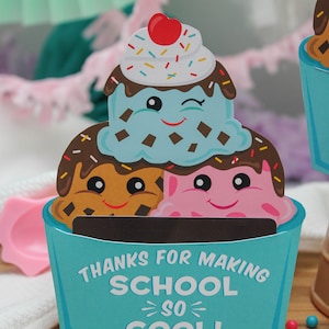 Puede incluir: Una tarjeta de cono de helado azul y blanco con el texto "Gracias por hacer la escuela tan genial! Con cari&ntilde;o, Sawyer". El cono de helado est&aacute; decorado con salsa de chocolate, chispas y tres caras de dibujos animados.