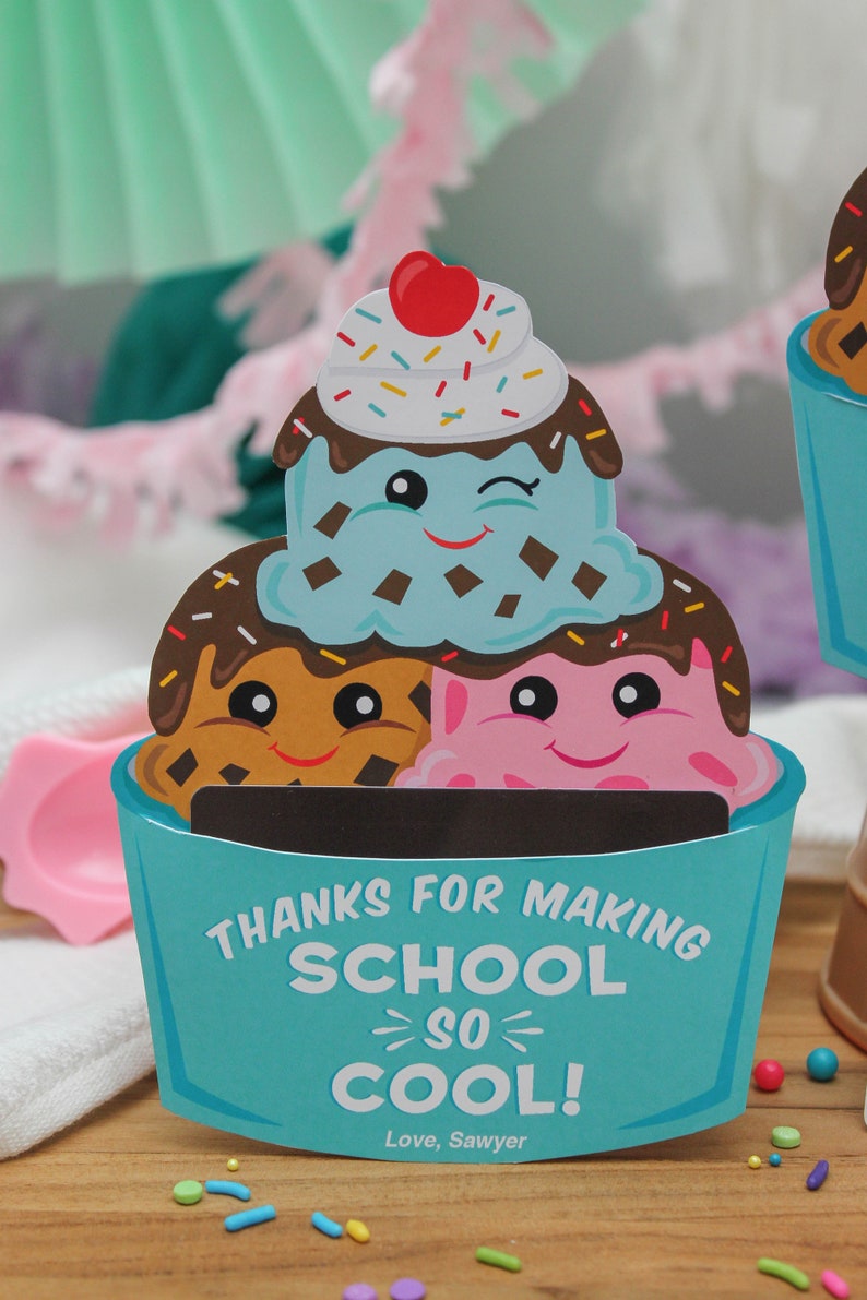 Puede incluir: Una tarjeta de cono de helado azul y blanco con el texto "Gracias por hacer la escuela tan genial! Con cari&ntilde;o, Sawyer". El cono de helado est&aacute; decorado con salsa de chocolate, chispas y tres caras de dibujos animados.