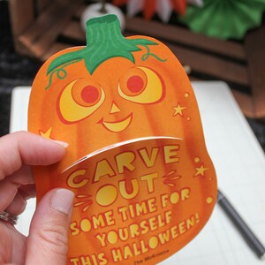 May include: A bright orange pumpkin-shaped card with a friendly face and the text "CARVE OUT SOME TIME FOR YOURSELF THIS HALLOWEEN! Love, The McKowns"