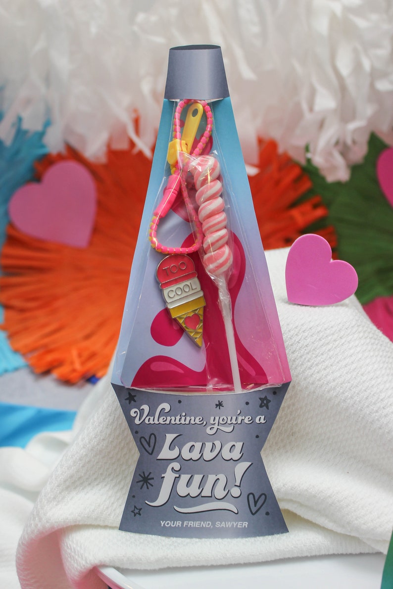Peut inclure: Une carte de Saint-Valentin avec une sucette en spirale rose et blanche, un charme de cr&egrave;me glac&eacute;e rose et bleu, et le texte "Valentine, you're a Lava fun!"  Your Friend, Sawyer.