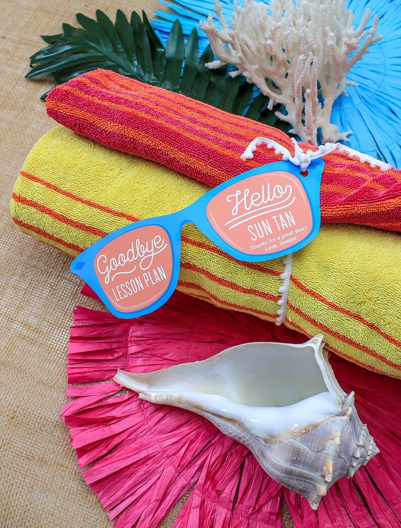May include: A pair of blue paper sunglasses with the words "Goodbye Lesson Plan" on one lens and "Hello Sun Tan Thanks for a great year! Love, Sawyer" on the other lens. The sunglasses are on top of two yellow and orange striped towels.