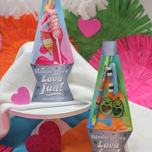 Peut inclure: Deux sacs cadeaux pour la Saint-Valentin en forme de lampes &agrave; lave. Les sacs sont remplis de petits cadeaux et portent un message qui dit "Valentine, you're a Lava Fun!"
