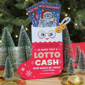Pode incluir: Uma meia vermelha com uma bainha branca e um rosto branco com &oacute;culos. A meia tem as palavras "LOTTO CASH" e "The stockings were hung by the chimney with care, in hopes that a lotto cash soon would be there! Love, The McKown Family" impressas nela. H&aacute; moedas de ouro espalhadas sobre uma superf&iacute;cie de madeira na frente da meia.