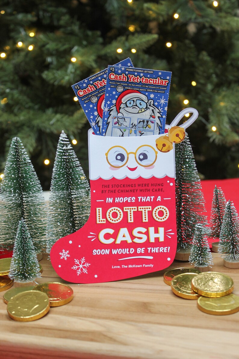 Pode incluir: Uma meia vermelha com uma bainha branca e um rosto branco com &oacute;culos. A meia tem as palavras "LOTTO CASH" e "The stockings were hung by the chimney with care, in hopes that a lotto cash soon would be there! Love, The McKown Family" impressas nela. H&aacute; moedas de ouro espalhadas sobre uma superf&iacute;cie de madeira na frente da meia.