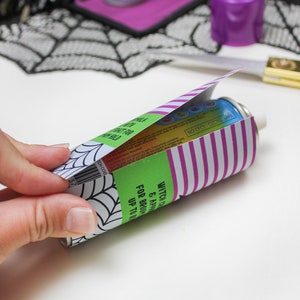 May include: A green and purple can with a spiderweb design and the text "Witch's Brew & Apple Cider" and "For Brooding Up To 14 Days". The can is partially covered with a pink and white striped paper.