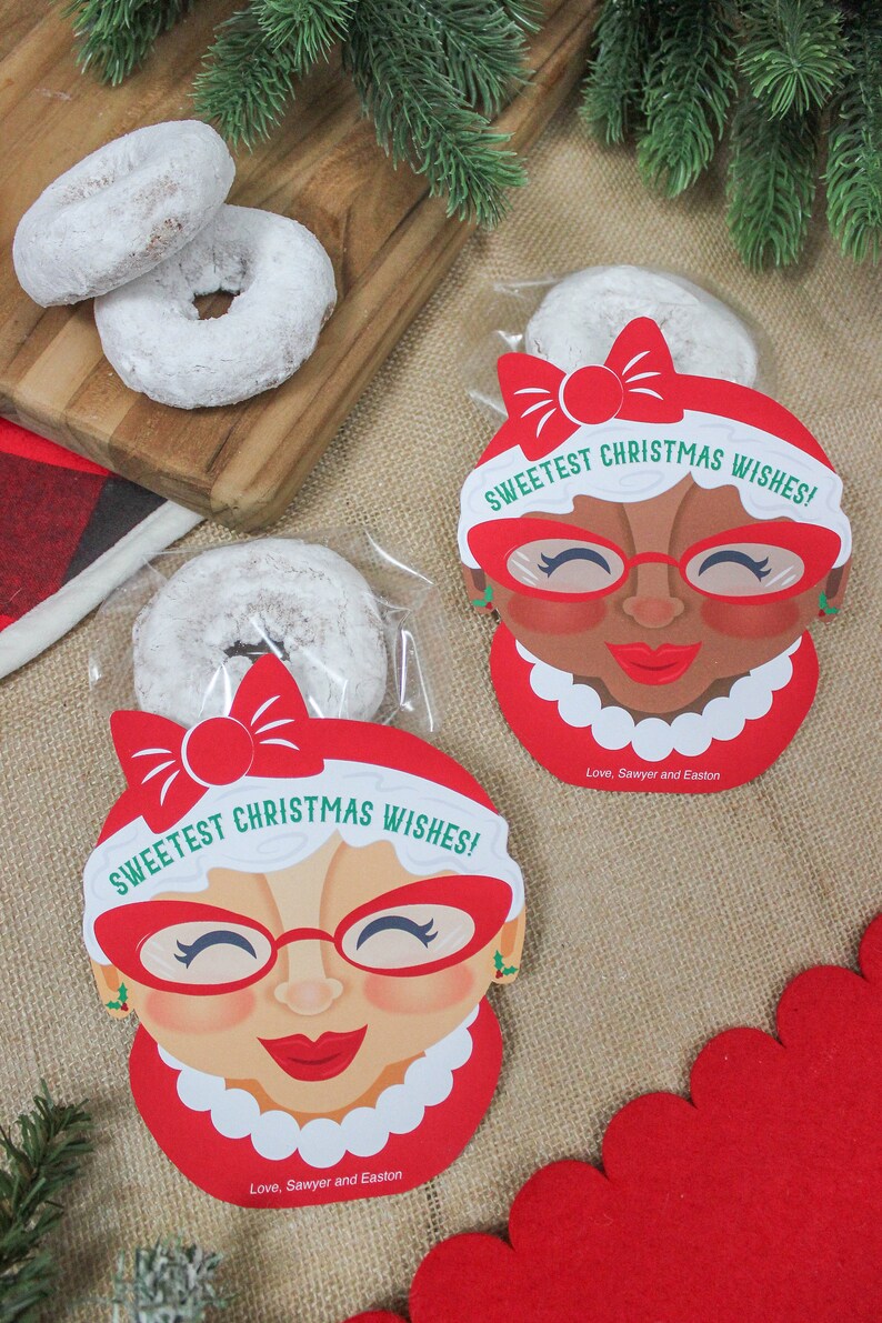 May include: Two clear plastic bags filled with powdered doughnuts and decorated with red and white Christmas-themed gift tags. The tags feature a cartoon woman wearing red glasses and a red bow. The text on the tags reads "Sweetest Christmas Wishes!" and "Love, Sawyer and Easton".