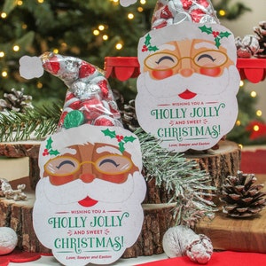 May include: Two festive Santa Claus gift bags with a red and white candy cane design. Each bag is filled with chocolate candies and has a message that reads "Wishing you a Holly Jolly and Sweet Christmas! Love, Sawyer and Easton".