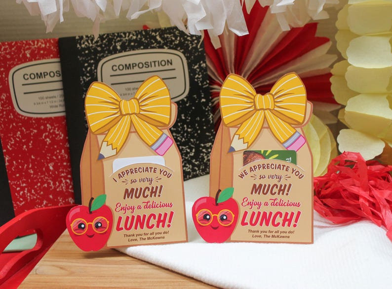 May include: Two brown paper lunch bags with yellow bows and pencils sticking out of the top. Each bag has a red apple with googly eyes and the text "I appreciate you so very much! Enjoy a delicious lunch! Thank you for all you do! Love, The McKownes" and "We appreciate you so very much! Enjoy a delicious lunch! Thank you for all you do! Love, The McKownes".