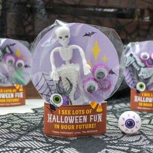 May include: A Halloween-themed goodie bag with a purple background and a skeleton toy, googly eyes, and a spider. The bag has a tag that says "I see lots of Halloween fun in your future!"