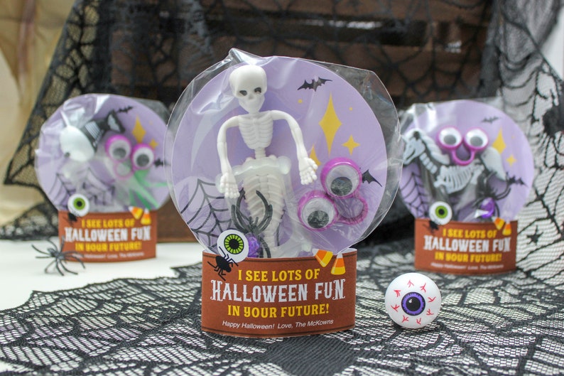 May include: A Halloween-themed goodie bag with a purple background and a skeleton toy, googly eyes, and a spider. The bag has a tag that says "I see lots of Halloween fun in your future!"