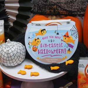 May include: A blue and white Halloween card with a goldfish bowl design. The card says "Hope you have a fin-tastic Halloween!" and features a goldfish with a witch hat. There are also goldfish crackers on a white plate.