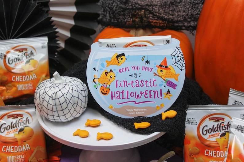 May include: A blue and white Halloween card with a goldfish bowl design. The card says "Hope you have a fin-tastic Halloween!" and features a goldfish with a witch hat. There are also goldfish crackers on a white plate.