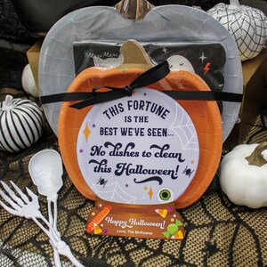 May include: A Halloween party favor gift basket with a pumpkin-shaped paper plate, a black and white striped paper plate, a ghost-shaped paper plate, a black and white spiderweb tablecloth, and two white plastic skeleton utensils. The pumpkin plate has a fortune teller design with the text "This fortune is the best we've seen... No dishes to clean this Halloween!" and a tag that says "Happy Halloween! Love, The McKowns".