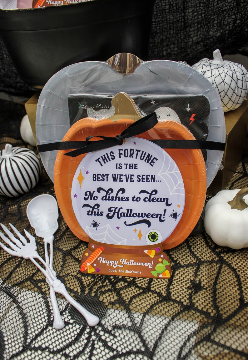 May include: A Halloween party favor gift basket with a pumpkin-shaped paper plate, a black and white striped paper plate, a ghost-shaped paper plate, a black and white spiderweb tablecloth, and two white plastic skeleton utensils. The pumpkin plate has a fortune teller design with the text "This fortune is the best we've seen... No dishes to clean this Halloween!" and a tag that says "Happy Halloween! Love, The McKowns".