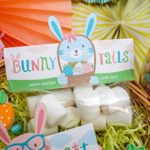 May include: A basket filled with Easter treats, including bags of marshmallows with bunny-themed tags that say "Bunny Tails" and "Bunny Bait". The tags are decorated with cartoon bunnies and the text "Happy Easter!" and "Love, Ella" and "Love, Sawyer".
