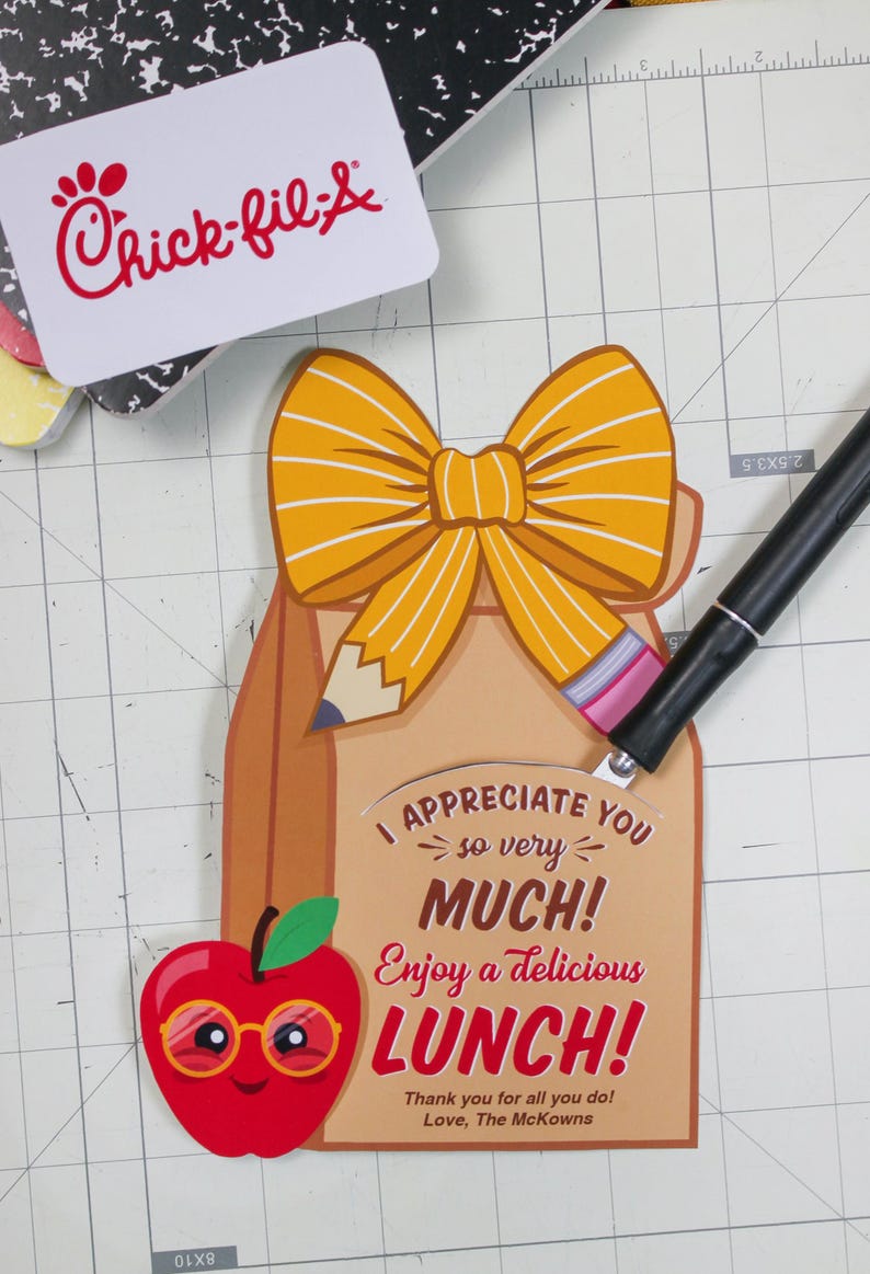 May include: A brown lunch bag with a yellow bow and a pencil sticking out of the top. The bag has a red apple with glasses on the front and the text "I appreciate you so very much! Enjoy a delicious lunch! Thank you for all you do! Love, The McKowns."