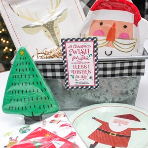 May include: A Christmas gift basket with a metal container, black and white checkered ribbon, and a card that reads "A Christmas Wish for you is to have a few less dishes to do!" The basket includes a variety of Christmas-themed paper plates, napkins, and a small green Christmas tree.