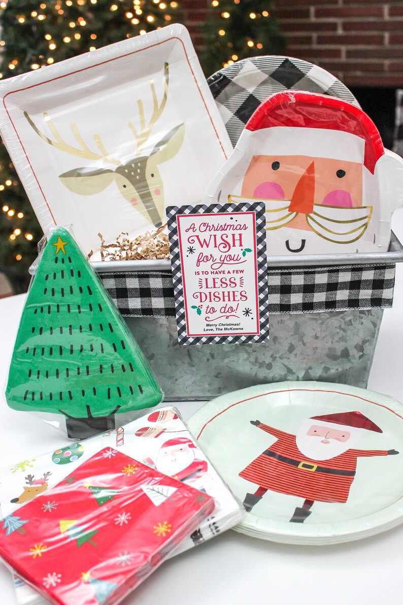 May include: A Christmas gift basket with a metal container, black and white checkered ribbon, and a card that reads "A Christmas Wish for you is to have a few less dishes to do!" The basket includes a variety of Christmas-themed paper plates, napkins, and a small green Christmas tree.