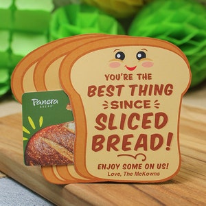 May include: A brown and yellow card shaped like a slice of bread with the text "You're the best thing since sliced bread!" and "Enjoy some on us! Love, The McKowns". A Panera Bread gift card is partially visible behind the card.